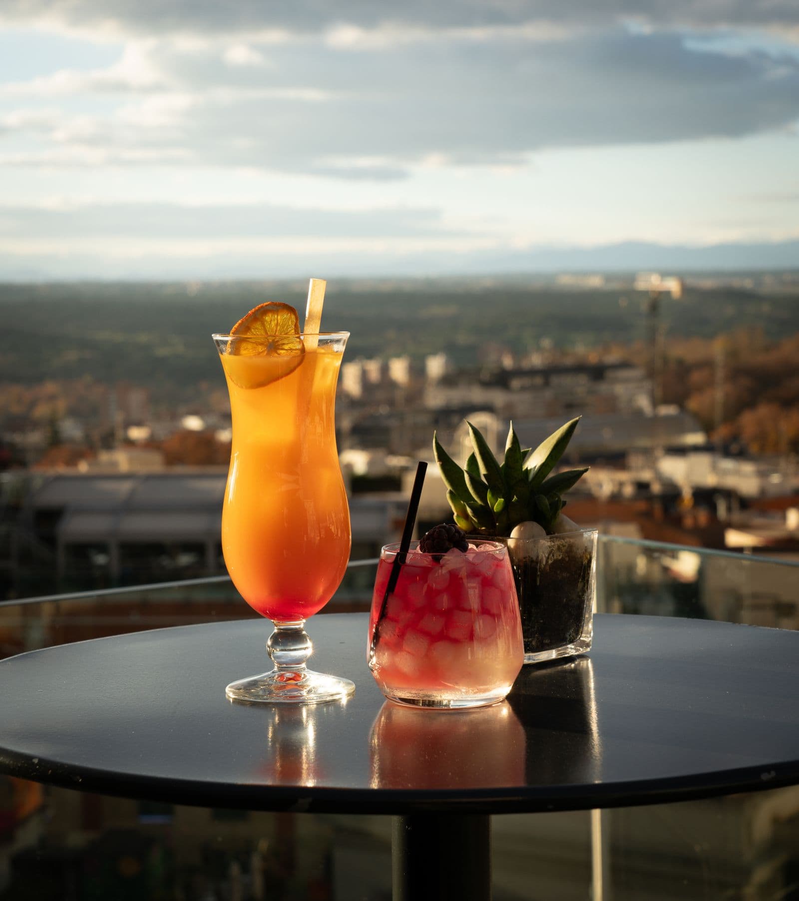Cocktails on a rooftop bar table overlooking the city at sunset
